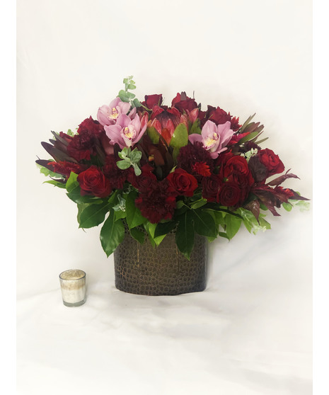 Cymbidium orchids, roses and more in shades of deep red and pink presented in a charming container.