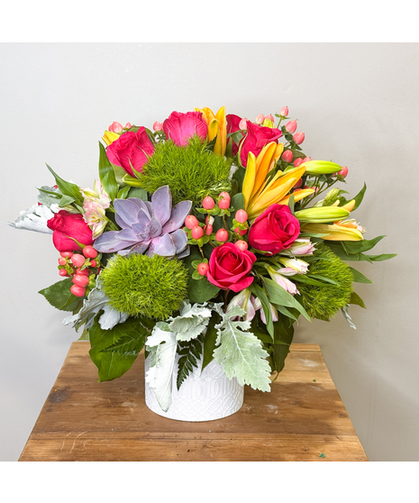 Peach roses, succulent blooms and lilies are paired in a ceramic container